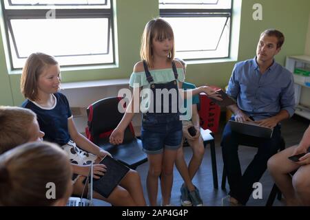 Grundschulmädchen stehen und sprechen mit Klassenkameraden Stockfoto