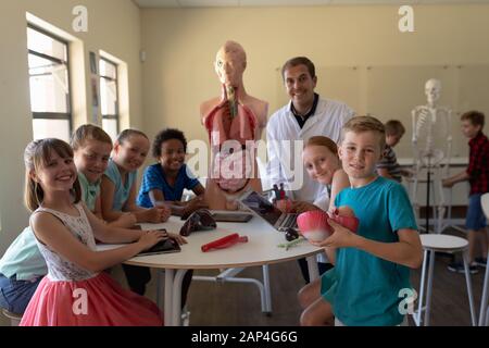 Männlicher Lehrer, der einen Labormantel und Schüler mit Anatomie-Modell trägt Stockfoto