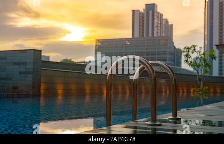 Swimmingpool im Luxushotel und Whirlpool am Morgen mit goldenem Sonnenaufgang. Leiter der Haltegriffe in der Nähe mit sauberem Wasser und Holzboden am Rand Stockfoto