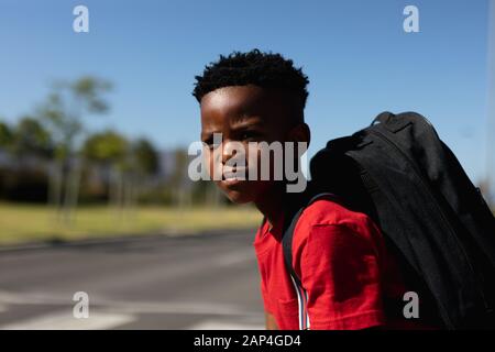Schuljunge, die auf der Suche nach Verkehrsbehinderungen sind, während sie auf die Straße warten Stockfoto
