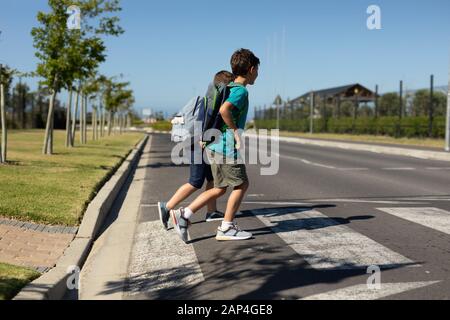 Zwei Schuljungen, die auf einem Fußgängerübergang die Straße überqueren Stockfoto