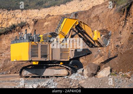 Der Laderbagger während der Erdbewegungsarbeiten lädt den Boden in einen großen gelben Kippwagen. Concept Open Mine Stockfoto