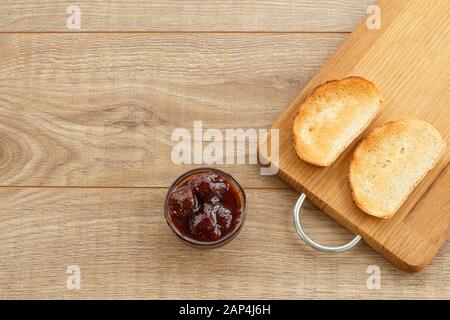 Hausgemachte Erdbeermarmelade in eine Glasschüssel und Toast auf Schneidebrett auf hölzernen Schreibtisch. Ansicht von oben. Stockfoto