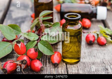 Glasflasche Rosehip ätherisches Öl mit frischen Rosehips auf einem Holztisch. Tinktur oder ätherisches Öl mit Rosenhüften. Heilkräutermedizin. Stockfoto