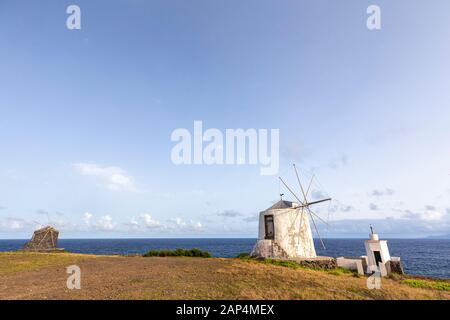 Berühmte Windmühlen und ein Meeresfeuer mit Flores in der Ferne nahe Vila do Corvo auf der Insel Corvo auf den Azoren, Portugal. Stockfoto