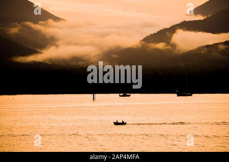 Morgenfrühaufgang Sonnenaufgang und Angelausbruch für den Tag im Hafen von Cairns mit Bergen und Nebelwolke, Cairns, Queensland, Australien Stockfoto