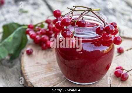 Glasbecher mit hausgemachter Viburnummarmelade mit frischen Viburnumbeeren auf einem Holztisch. Quelle natürlicher Vitamine. In der Volksmedizin verwendet. Herbsternte. Stockfoto