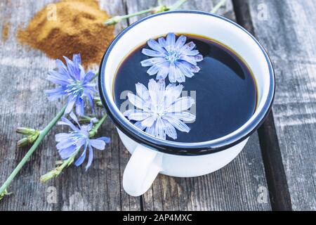 Weißer Becher mit Zichoriengetränk und Blumen in der Nähe von Zichorienpulver. Tee aus der Zichorie. Gesundes Esskonzept. Kaffee-Ersatz. Stockfoto