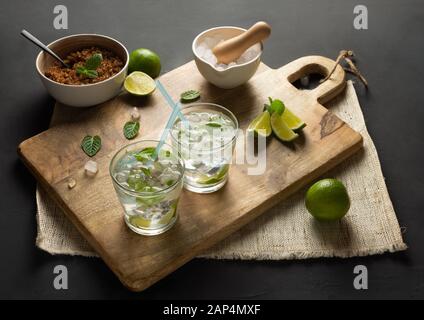 Caipirinha von Cachaça, Mojito aus weißem Rum, Kalk, frischer Minze, braunem Zucker und zerkleinertem Eis. Rustikale Umgebung mit schwarzem Hintergrund Stockfoto