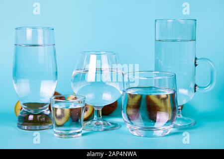 Brille unterschiedlicher Form mit Wasser auf blauem Grund. Kiwi im Hintergrund. Stockfoto