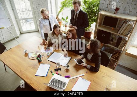 Positiv ist. Gruppe junger Geschäftsleute in einer Sitzung. Vielfältige Gruppe von Kollegen diskutieren neue Entscheidungen, Pläne, Ergebnisse, Strategie. Kreativität, Arbeitsplatz, Unternehmen, Finanzen, Teamarbeit. Stockfoto
