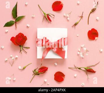 Weißer Geschenkkasten und rote Rosen auf hellrosa Hintergrund Draufsicht Stockfoto