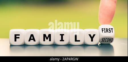 Die Hand dreht einen Würfel und ändert den Ausdruck "Familie an zweiter Stelle" in "Familie an erster Stelle". Stockfoto