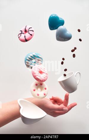 St. Valentin Konzept, Levitation der Krapfen oben Herzförmige Schale. Kaffee Bohnen fliegen in Espresso Tasse. Hand balancing Kaffeetasse am Finger. Creativ Stockfoto