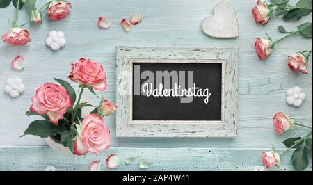 Ansicht von oben, Text 'Valentinstag' auf Tafel in deutscher Sprache bedeutet "Valentinstag". Rosa Rosen auf Hellblau mint Hintergrund mit Herzen und Tafel. Stockfoto