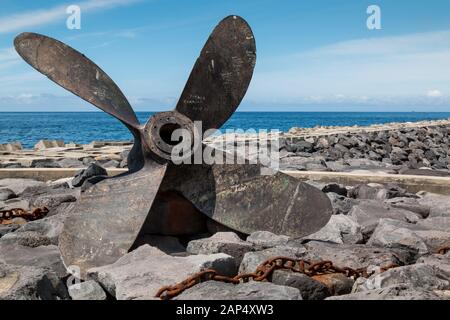 Boot Propeller, im Hafen als Statue verwendet. An der felsigen Küste, im Atlantik im Hintergrund. Blauer Himmel mit weißen Wolken. Povoacao, Sao Miguel, Azoren Stockfoto