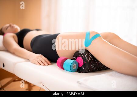 Patientin mit verletzten Knie liegen auf einer Prüfung Tabelle während der KINESIOLOGISCHEN Behandlung. Kinesio tape, Physikalische Therapie, Rehabilitation Hintergrund Stockfoto