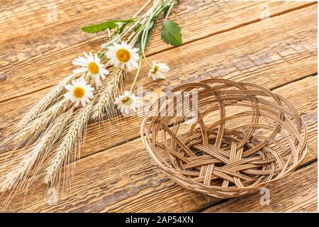 Weidenkorb, Blumenstrauß aus Kamillenblüten und trocken ährchen von Weizen auf alten Brettern. Ansicht von oben. Stockfoto