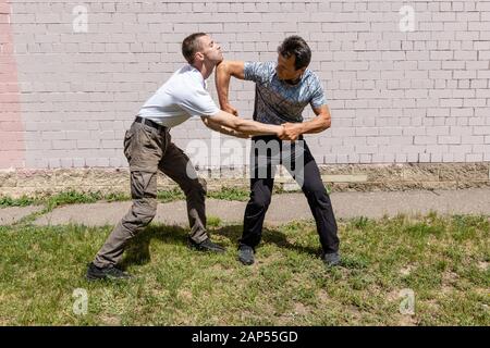 Reifer männlicher Ausbilder schlägt mit einem Angreifer in einen Ellenbogen. Selbstverteidigungsmethoden Krav Maga Stockfoto