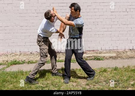 Reifer männlicher Ausbilder schlägt einem Angreifer ins Gesicht. Selbstverteidigungsmethoden Krav Maga Stockfoto