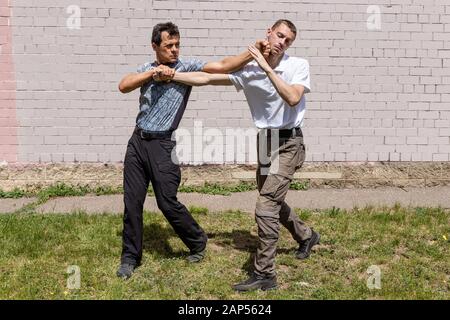 Ein reifer männlicher Ausbilder schlägt dem Angreifer mit der Faust ins Gesicht. Selbstverteidigungsmethoden Krav Maga Stockfoto