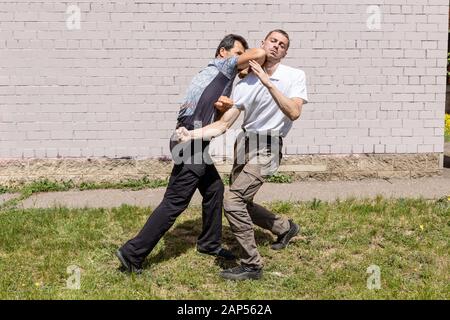 Ein reifer männlicher Ausbilder schlägt einem Angreifer einen Ellbogen im Kiefer zu. Selbstverteidigungsmethoden Krav Maga Stockfoto