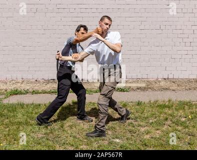 Reifer männlicher Ausbilder schlägt einem Angreifer mit einem Messer ins Gesicht. Selbstverteidigungsmethoden Krav Maga Stockfoto