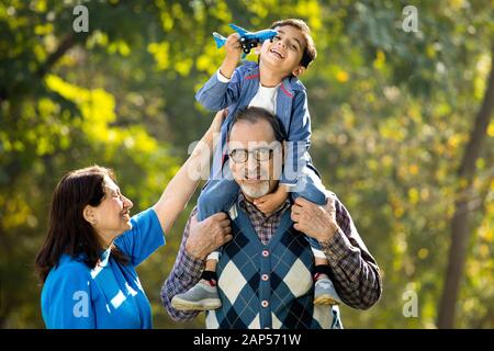 Großmutter mit Junge, die ein Spielzeugflugzeug auf der Schulter des Großvaters im Park hält Stockfoto