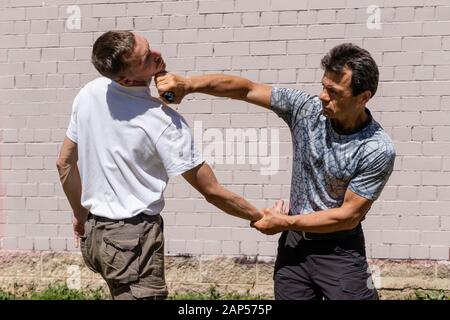 Verteidiger verteidigt sich mit einer Waffe gegen den Angreifer. Ein Mann schlägt dem Aggressor mit einer Pistole entgegen, die er ihm abnahm. Nahaufnahme. Selbstverteidigung Techniq Stockfoto