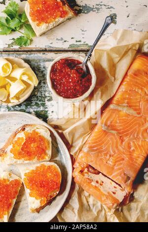 Roter Lachskaviar in Schale und auf Weizen Brot, Lachs Terrine serviert mit Butter auf Keramikplatte über alten Holztisch. Flach, Raum Stockfoto