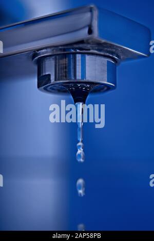 Aus einem Wasserhahn strömt ein Tropfen Wasser gegen eine blaue Kachel. Stockfoto
