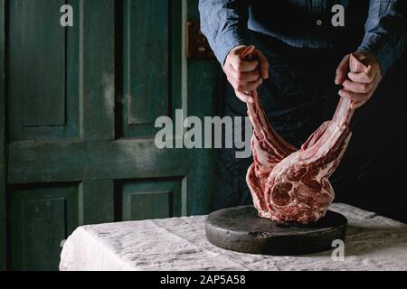 Des Menschen Hände halten Roh ungekocht Black Angus Rind tomahawk Steaks auf Knochen auf Leinen Tischdecke. Im rustikalen Stil Stockfoto