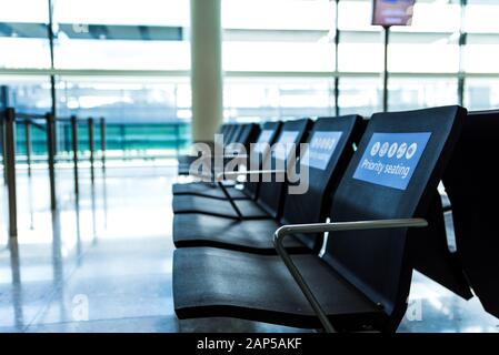 Leere Prioritätssitze an einem Flughafen im Wartebereich vor dem Einsteigen. Blaue Schilder auf Stühlen Stockfoto