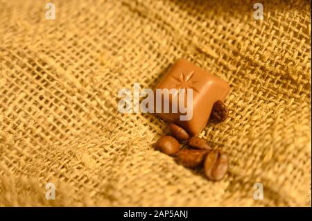 Schokolade und Kaffeebohnen auf dem Hintergrund rauer Homespun-Qualität. Nahaufnahme Stockfoto