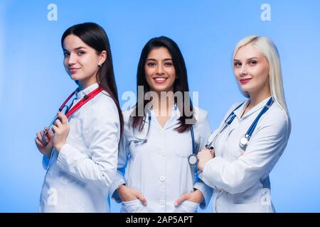 Ein Team junger Ärzte. Multinationale Menschen - Arzt, Krankenschwester und Chirurg in blauem Hintergrund. Eine Gruppe von Medizinstudenten verschiedener Nationalitäten a Stockfoto