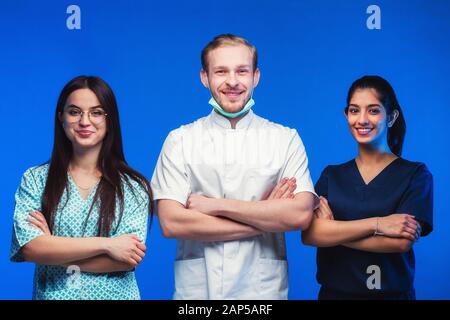 Ein Team junger Ärzte. Multinationale Menschen - Arzt, Krankenschwester und Chirurg in blauem Hintergrund. Eine Gruppe von Medizinstudenten verschiedener Nationalitäten a Stockfoto