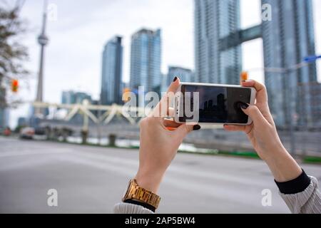 Mädchen, die mit dem Handy ein Bild vom CN Tower und dem Stadtbild von Toronto machen. Halten Sie das Smartphone mit den Händen Stockfoto