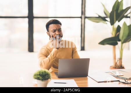 Fokussierter afro-Mann, der zu Hause mit einem Laptop arbeitet Stockfoto