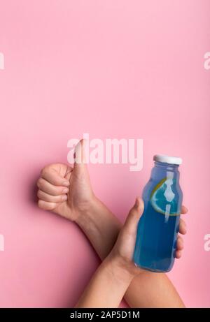 Frau zeigt Daumen hoch und hält Flasche mit köstlichem blauem Entgiftungswasser Stockfoto