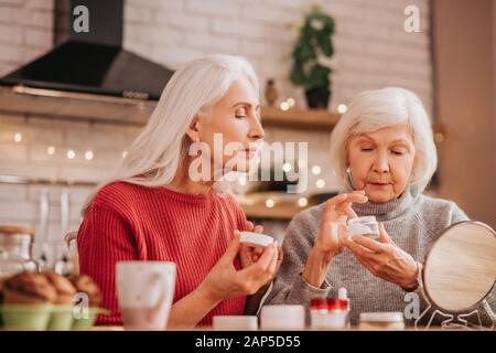 Zwei gut aussehende ältere Frauen die Anwendung neuer Creme Stockfoto