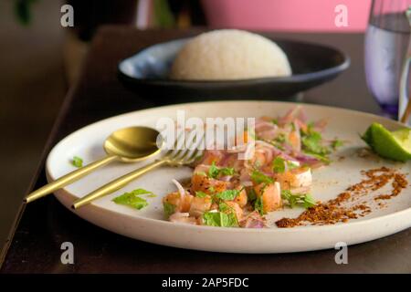 Gewürfelter roher Lachs mit roten Zwiebeln, Zitrone und Minze, mit gedämpftem Reis auf der Seite. Nahaufnahme. Stockfoto