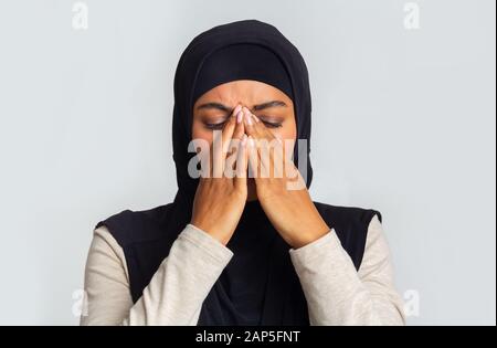 Verärgerte schwarze muslimin in Hijab, die Gesicht mit Händen bedeckt Stockfoto