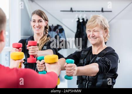 Ältere und junge Frau mit Hanteln in drahtlosen ems Fitnessraum Stockfoto