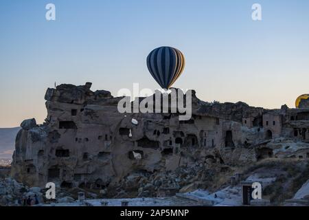 Kappadokien, Türkei: Heißluftballons im Morgengrauen auf der Kirche St. Johannes der Täufer (Burg Cavusin), berühmte Höhlenkirche aus dem 5. Jahrhundert auf dem Hügel Stockfoto