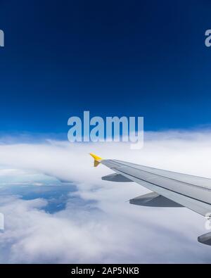Ansicht des Flügels von einem Flugzeug über den Wolken in großer Höhe fliegen unter einem blauen Himmel durch das Fenster auf der Beifahrerseite. Im Flug über Europa. Anzeigen von je Stockfoto