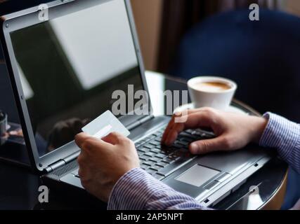 Man Hands machen Online-Shopping mit einer Kreditkarte auf dem Tisch in einem Restaurant. Mann Hand hält Kreditkarte und tippt auf einer Laptop-Tastatur Stockfoto
