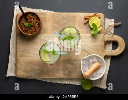 Caipirinha, Limette, frische Minze, brauner Zucker und zerkleinertes Eis. Rustikale Umgebung mit schwarzem Hintergrund. Luftansicht Stockfoto