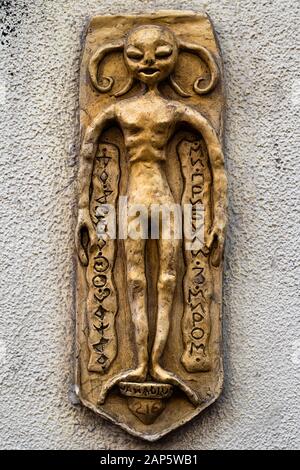 Alte goldene Statuette in Form eines mythischen Humanoiden. Alte fremde Figur an der Wand mit seltsamen und geheimnisvollen Symbolen. Tonprodukt Stockfoto