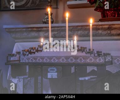 Kerzen, die von Gläubigen vor einem kleinen Altar in einer Kirche angeboten Stockfoto