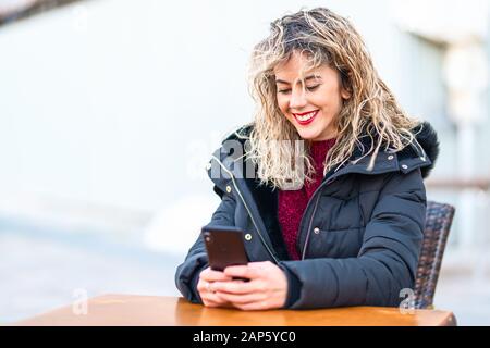 Schöne cacuasianische Frau, die einen Nachrichtentex mit Smartphone tippt. Girl Blonde lockiges Haar mit Platz für Text Stockfoto